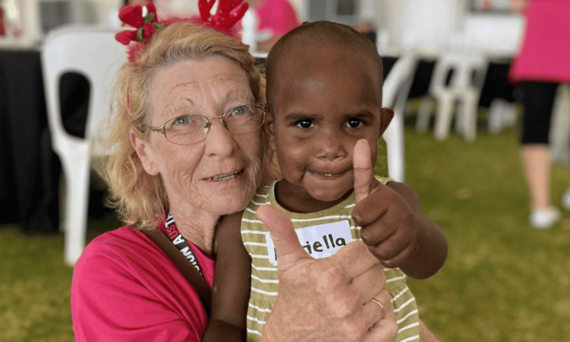 A volunteer wearing festive antlers holds a young child during the Christmas Lunch in the Park event.